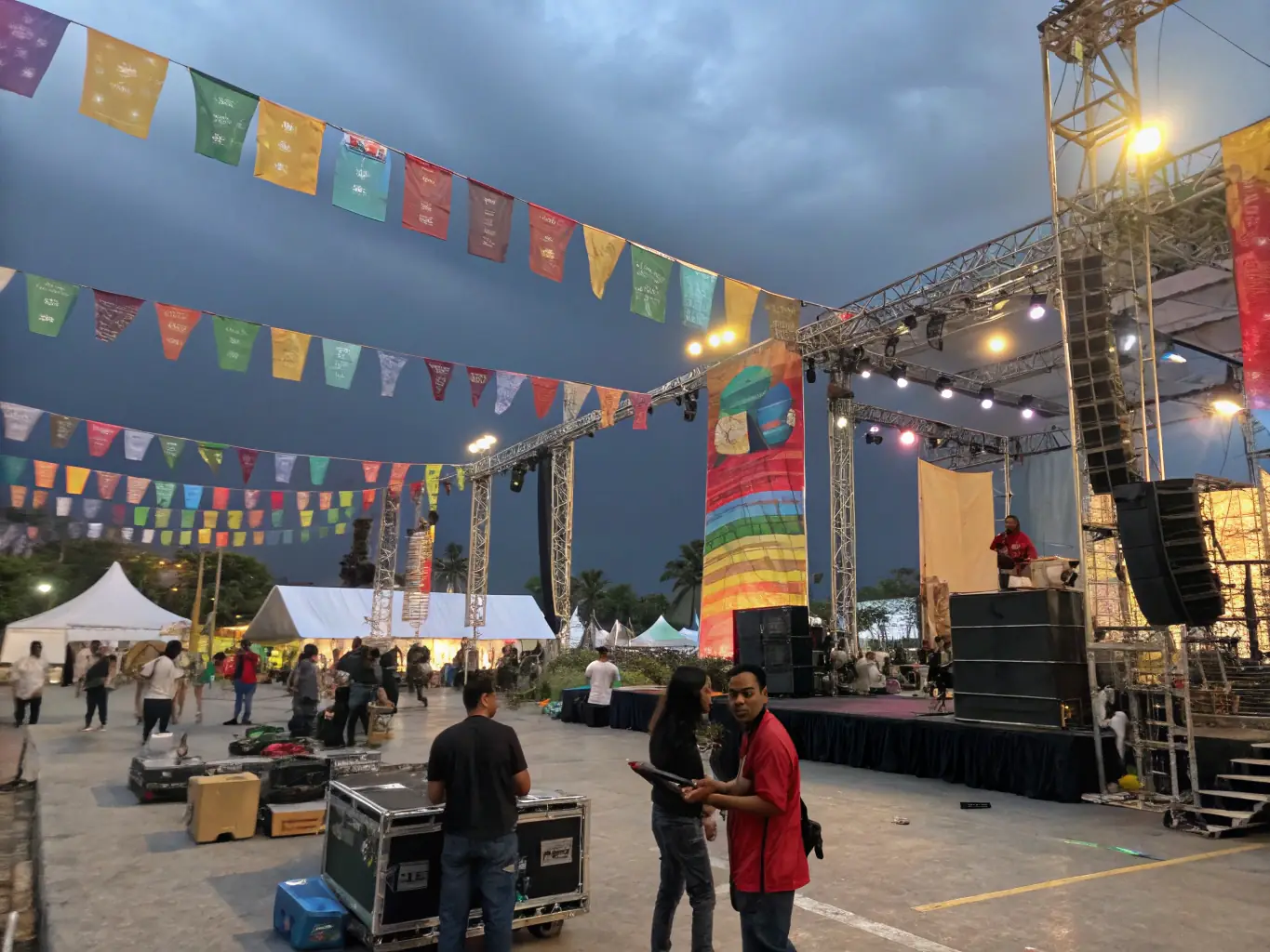 A wide shot of a stage setup with various pieces of stage technology, including rigging, video screens, and special effects equipment, set in a large event venue during setup.